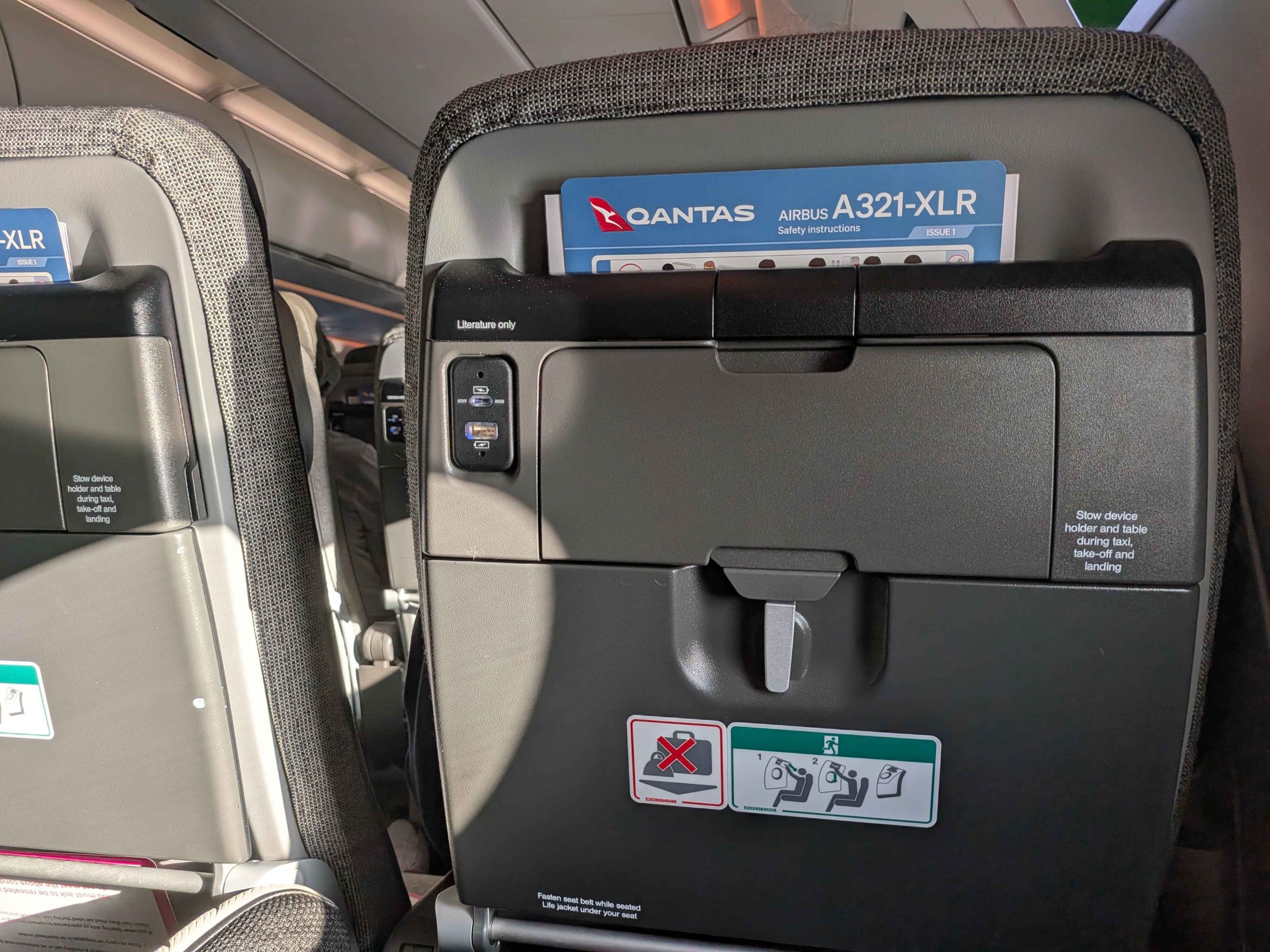 Qantas A321-XLR seat back showing USB-A and USB-C charging ports, tray table and safety card